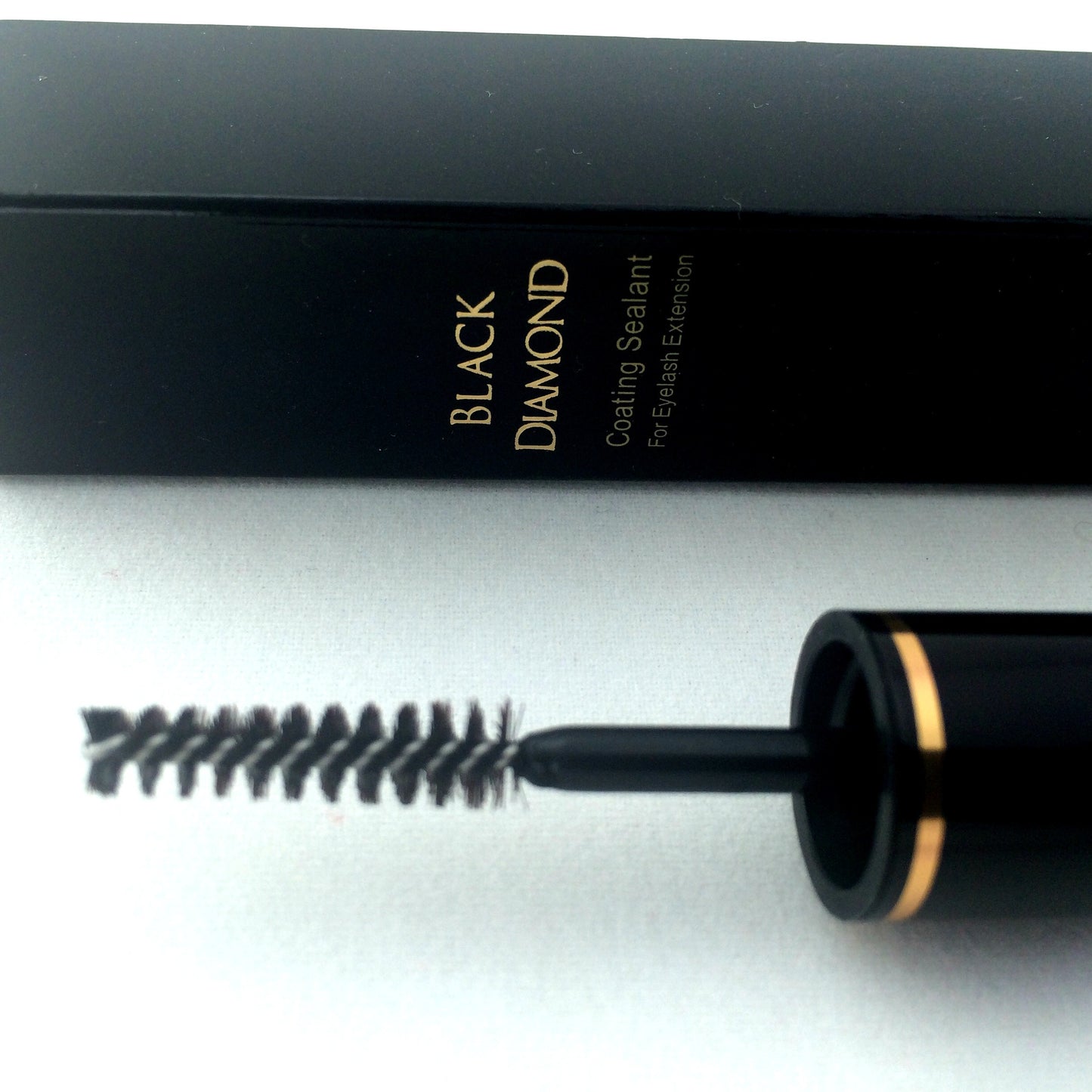 close up of Blink Black Diamond Eyelash Extension Sealant brush with packaging in the background